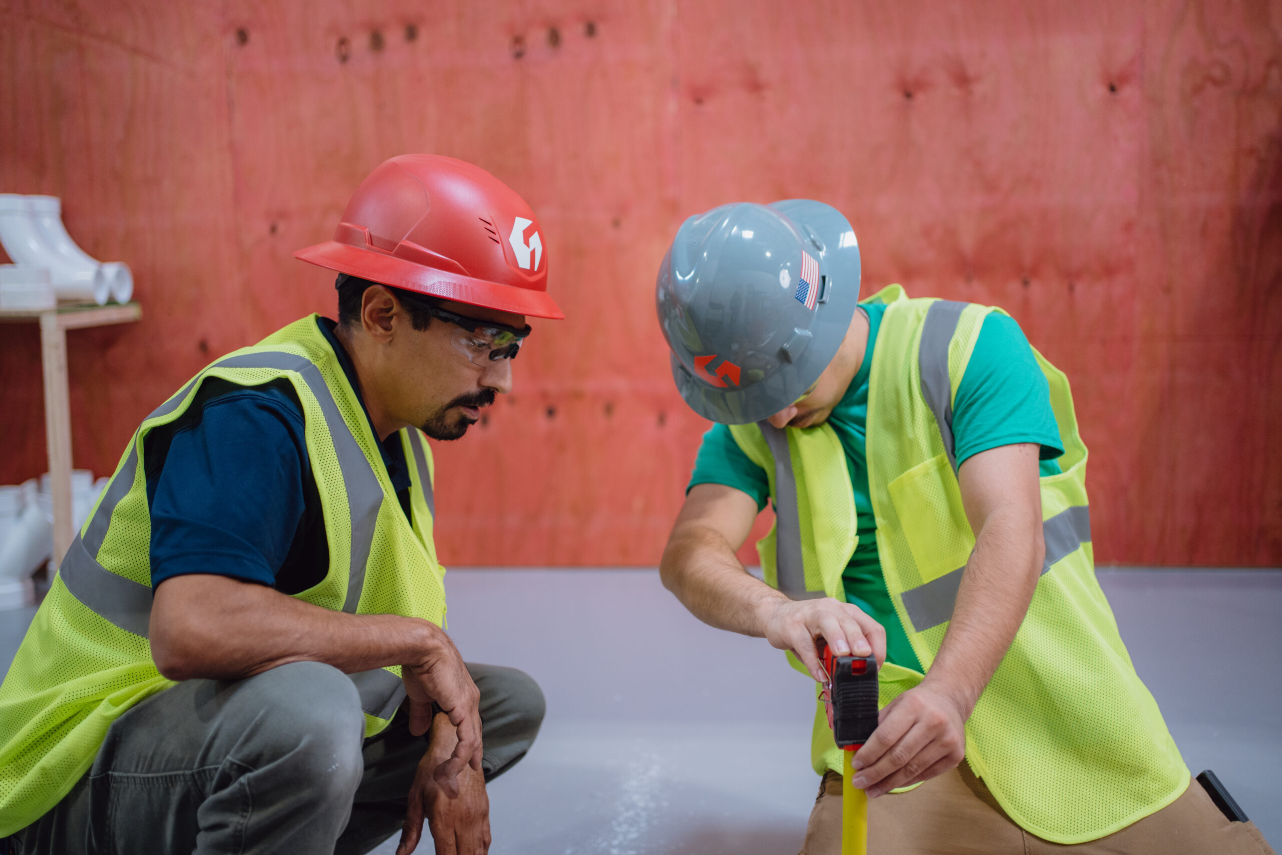 Two Tradecraft plumbing students in safety gear measuring pipe fittings in the San Antonio lab
