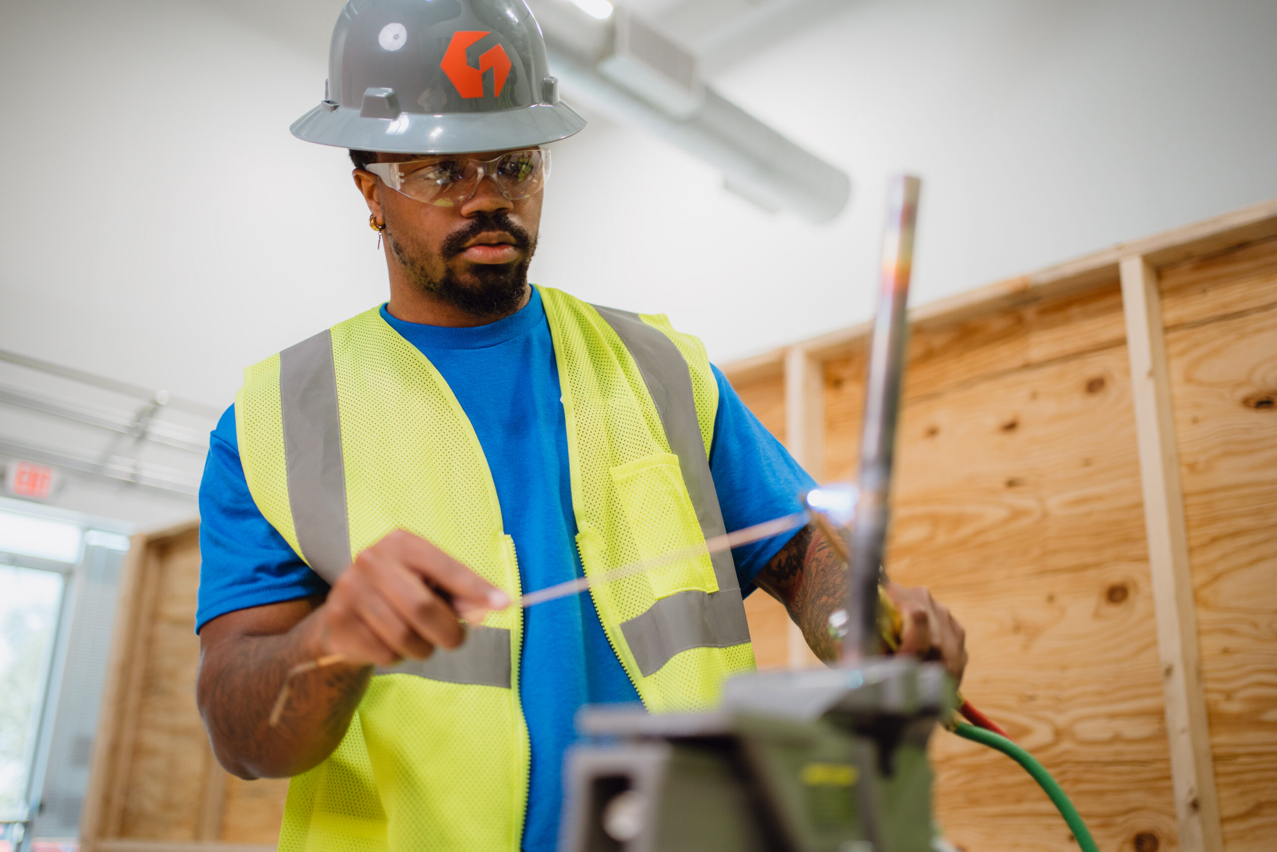 Focused Tradecraft HVAC student wearing safety glasses and a gray hard hat brazing copper tubing during hands-on lab training