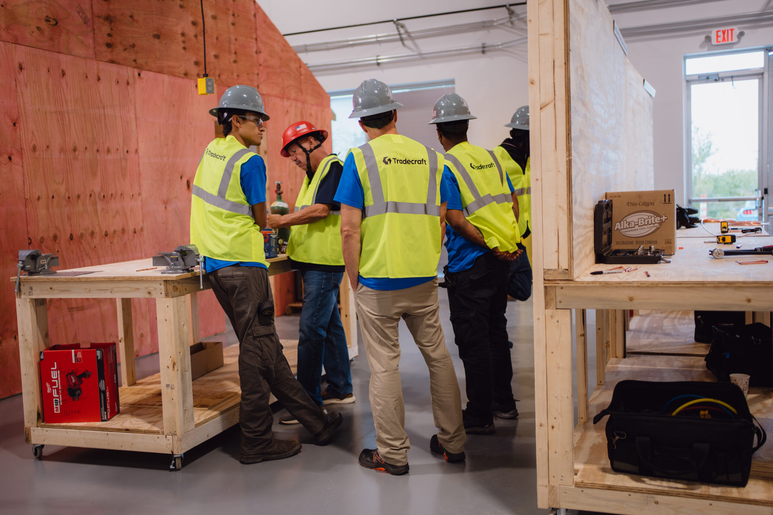 Tradecraft HVAC instructor and students in safety vests collaborating in framed lab booths at the San Antonio campus
