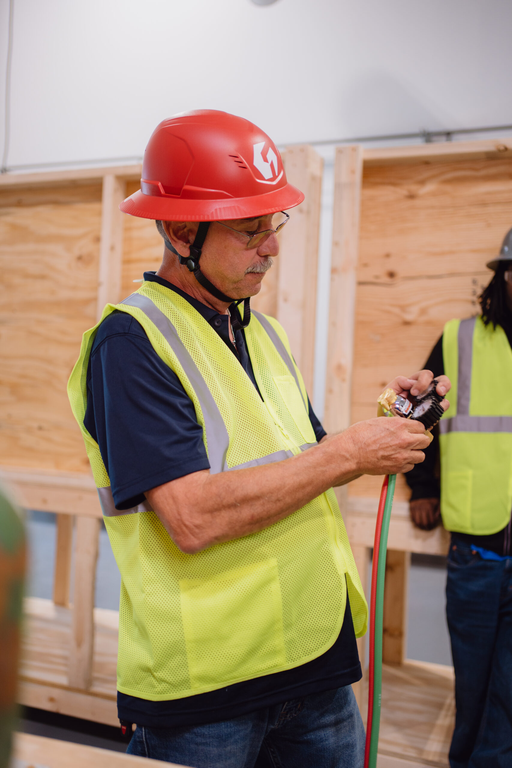 Tradecraft HVAC instructor in a red hard hat adjusting oxygen and acetylene torch regulator gauges during hands-on brazing instruction
