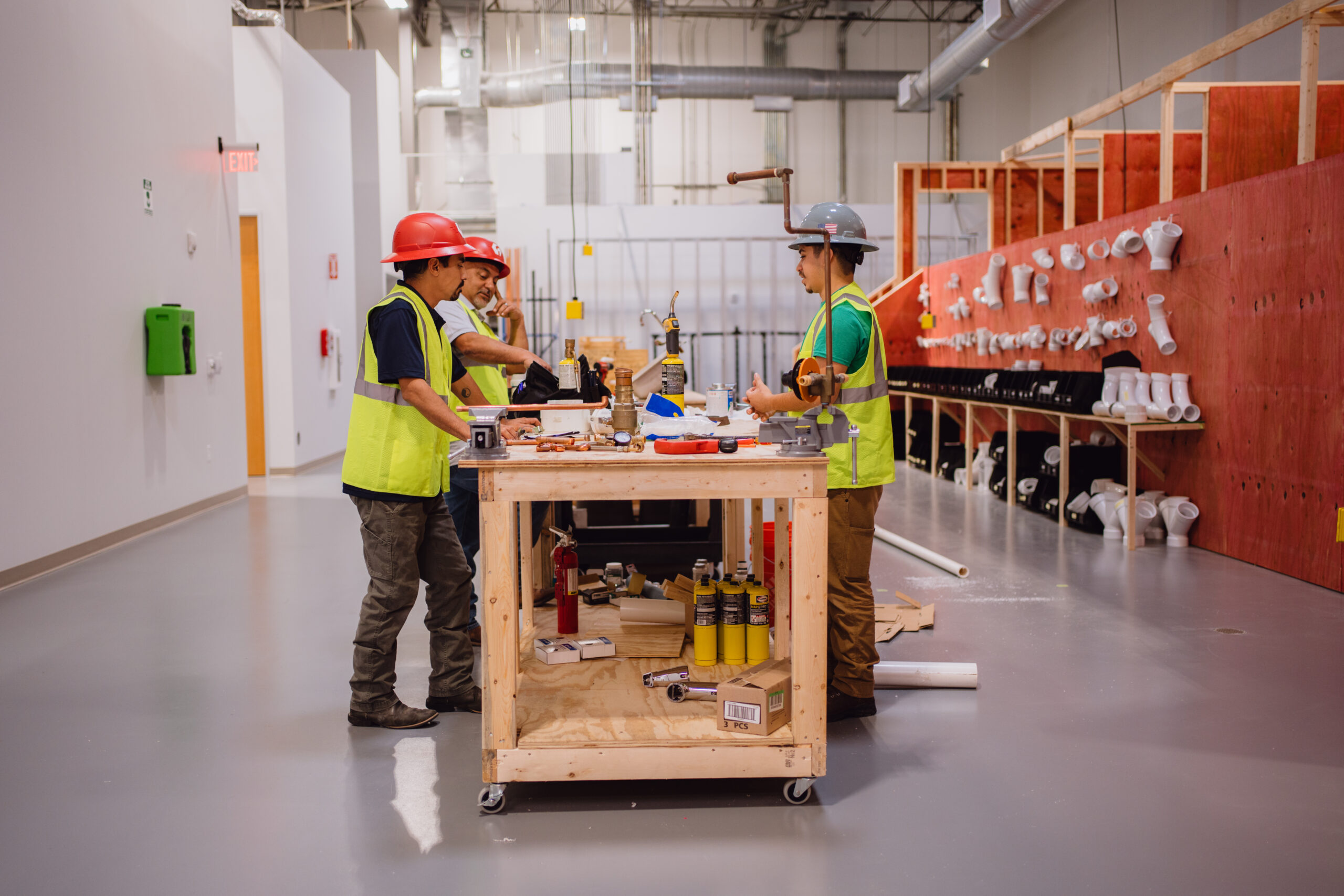 Tradecraft plumbing students collaborating around a mobile workbench in the San Antonio training facility