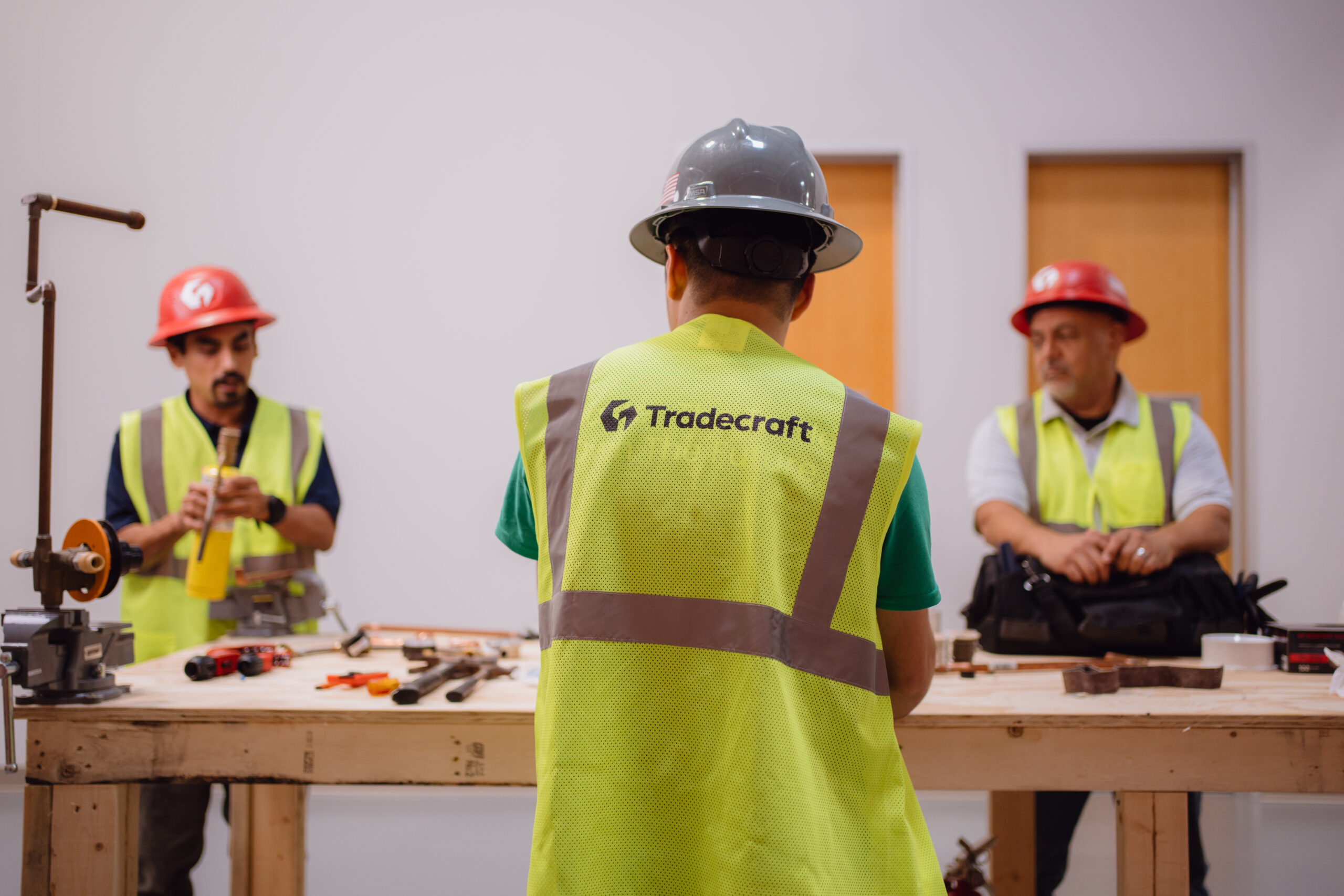 Tradecraft student in high-visibility safety vest watching an instructor demonstrate copper fitting techniques in San Antonio